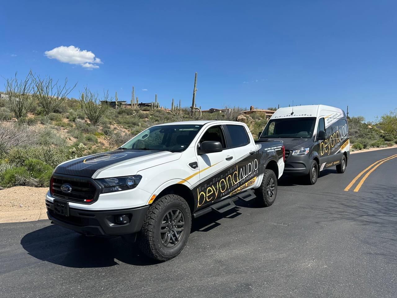 Beyond Audio service truck and van parked in the Sonoran desert outside a Scottsdale luxury home — both vehicles wrapped with the Beyond Audio Engineered Environments branding.