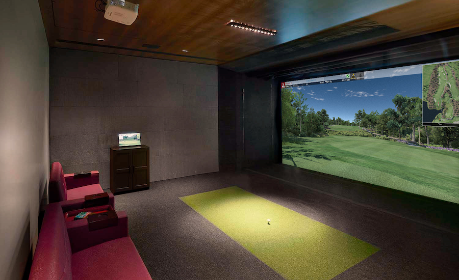 A home theater with a golf simulator and a green carpet.