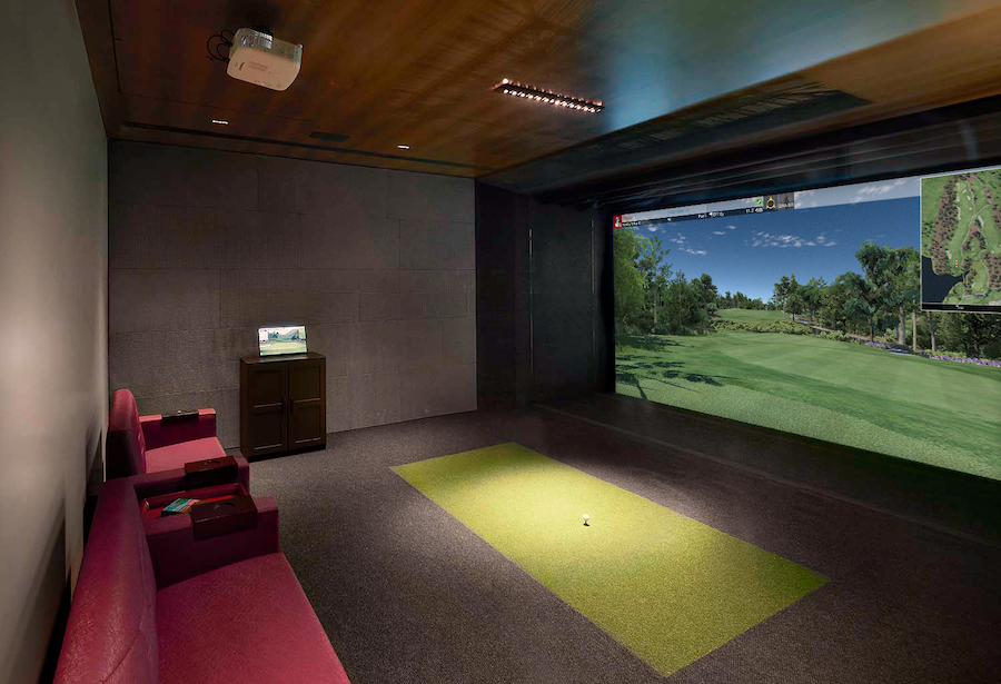 A home theater with a golf simulator and a green carpet.