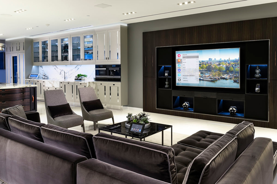 An open living room and kitchen with Crestron smart home touchscreens and the system displayed on the TV.