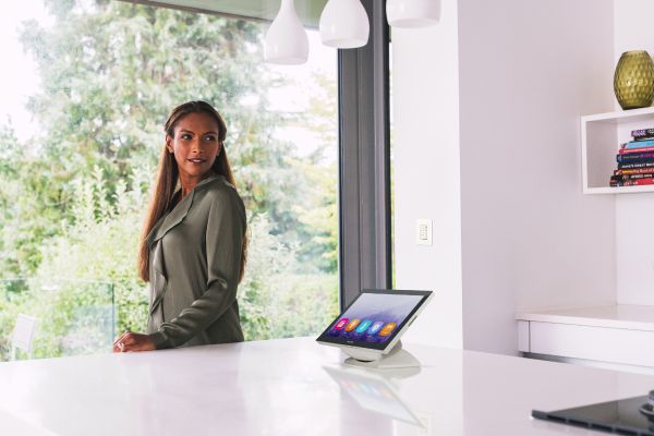 A woman standing by a window with a Crestron touchscreen on the kitchen counter.